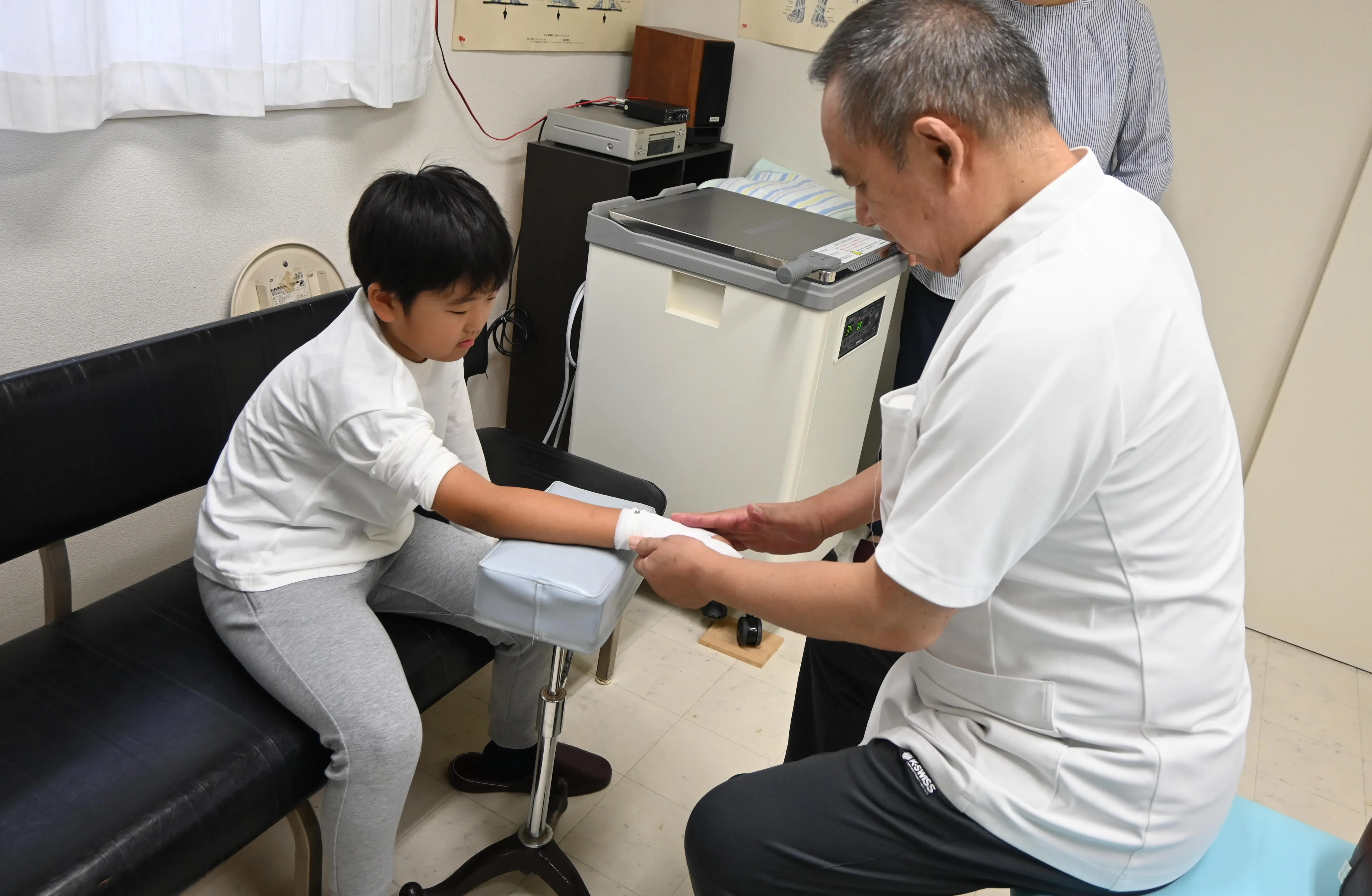 写真：子供に先生が包帯を巻いています。